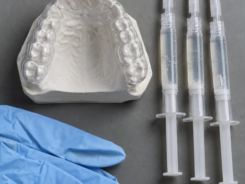 Moldeira de clareamento sobre o modelo de gesso ao lado das seringas de gel para o clareamento caseiro