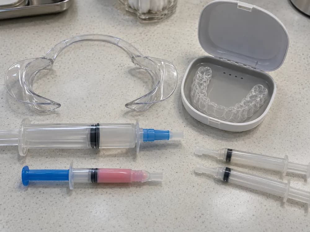 Kit de consultório e kit caseiro lado a lado: afastador, seringas de gel clareador e moldeira no estojo
