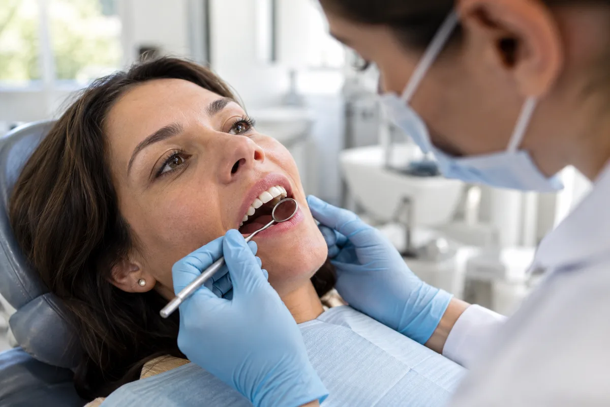 Dentista observando de perto o sorriso de uma paciente para avaliar o contorno da gengiva. Tudo para explicar gengivoplastia.